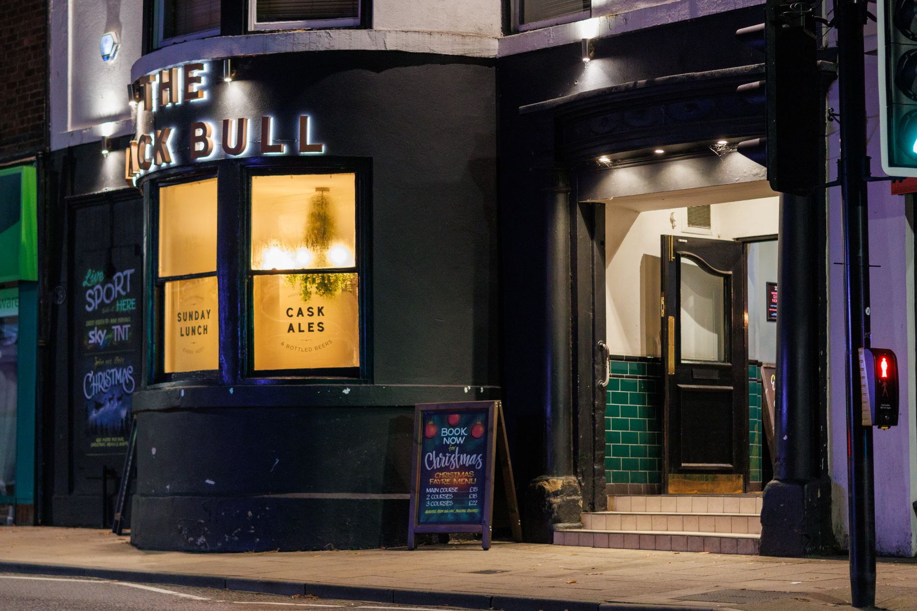 A warm and inviting pub exterior at night, showcasing signage and illuminated interior.