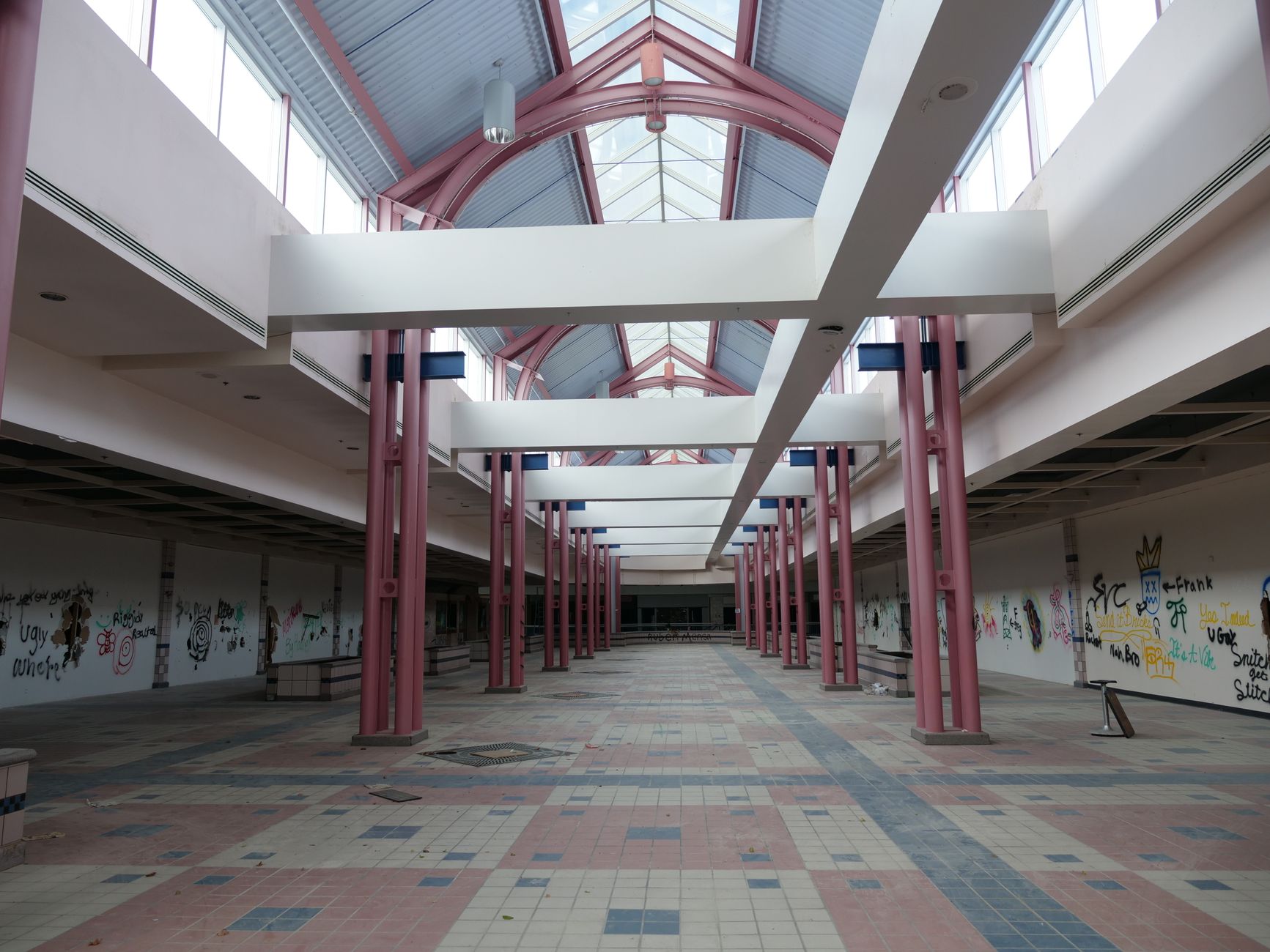 Desolate interior of an abandoned shopping mall with graffiti-covered walls.