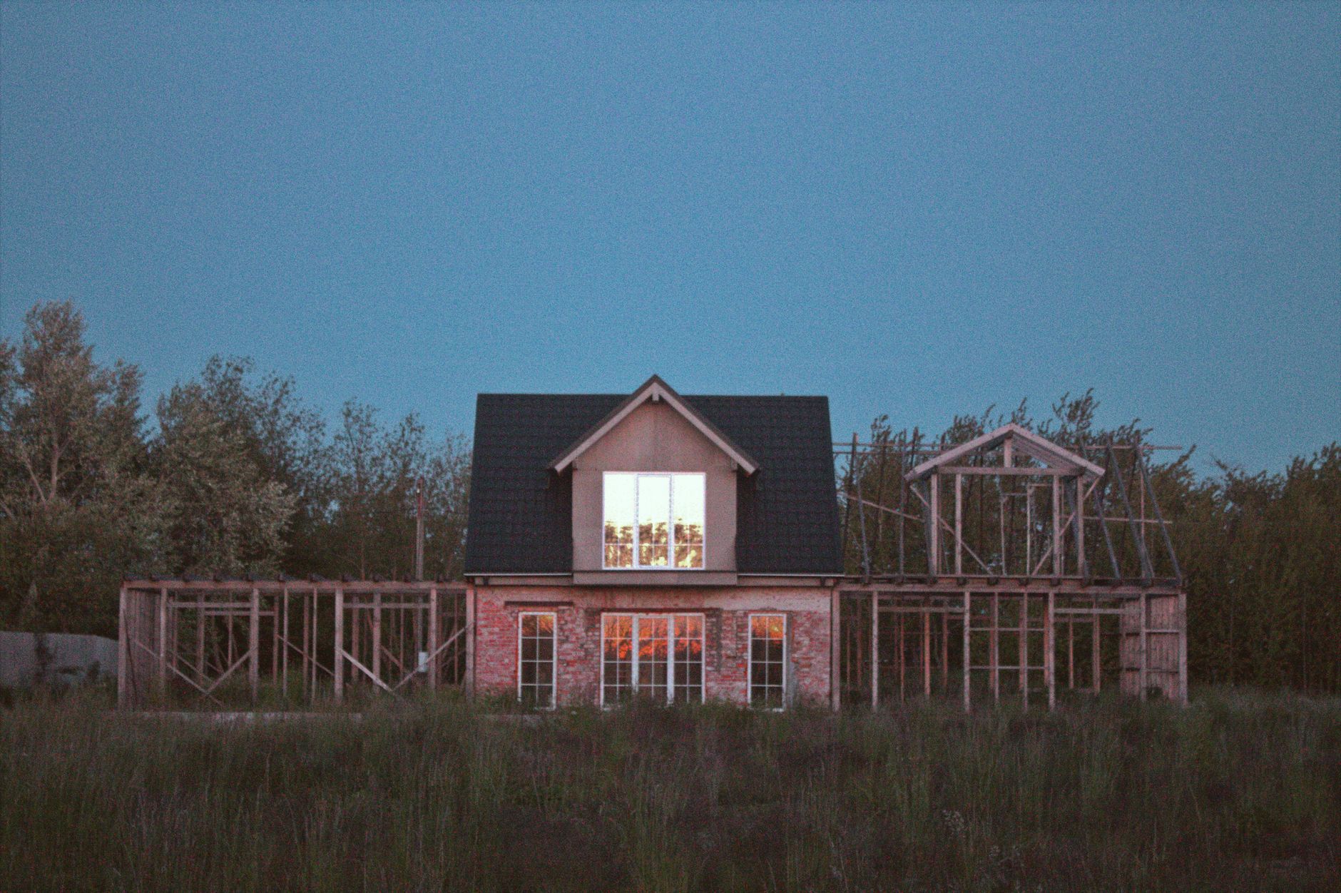 A half-constructed wooden house stands in a field during twilight.