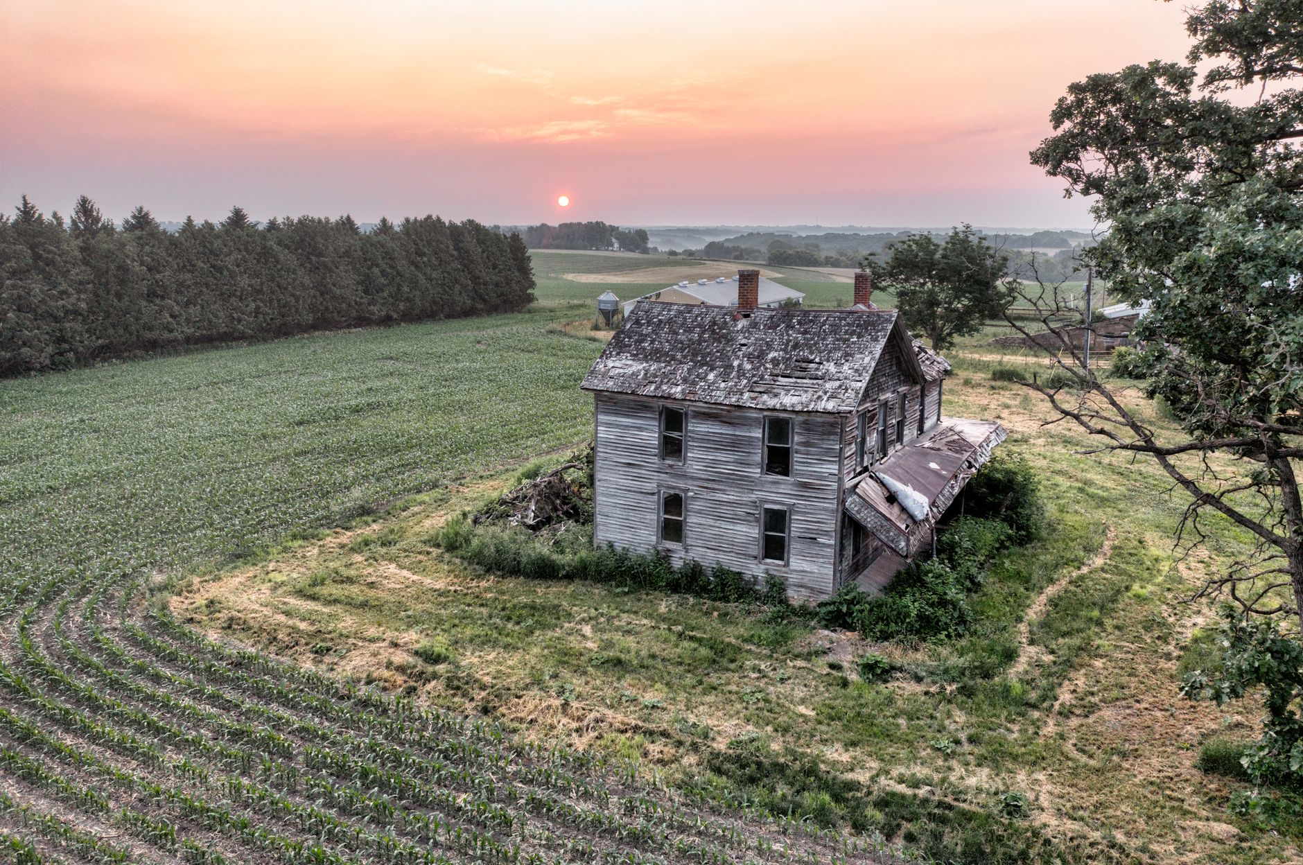 An aerial view of an abandoned farmhouse amidst rural fields at sunset in West Albany, Minnesota.