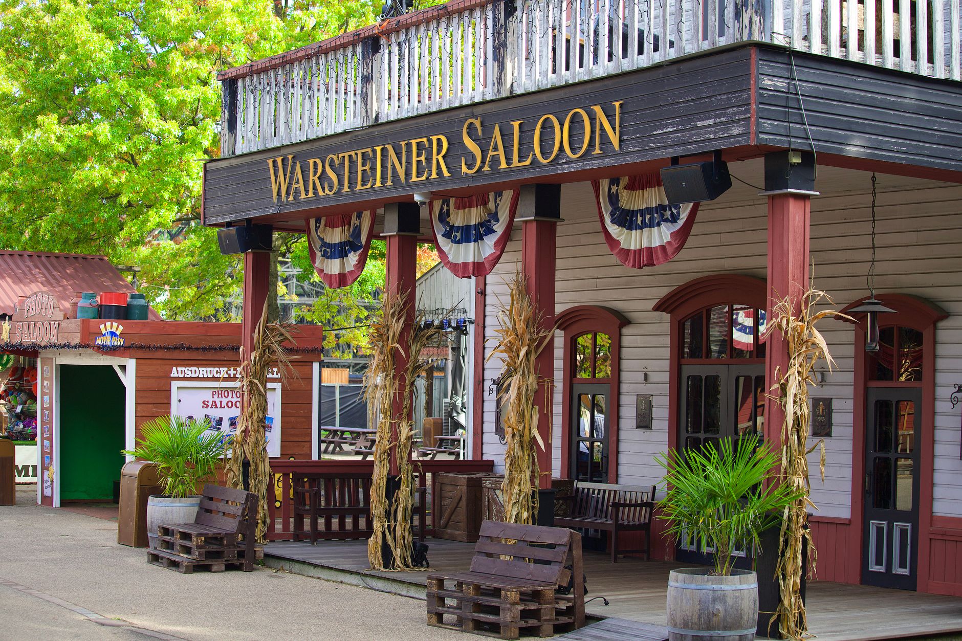 Historic Warsteiner Saloon with rustic decor, plants, and flags in a Western theme park setting.