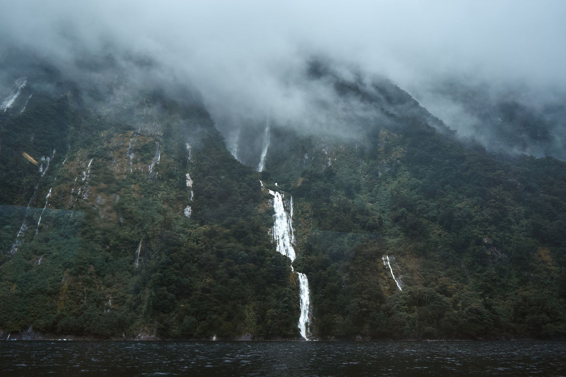 Foggy landscape of waterfalls in Fiordland, New Zealand, capturing nature's serene beauty.