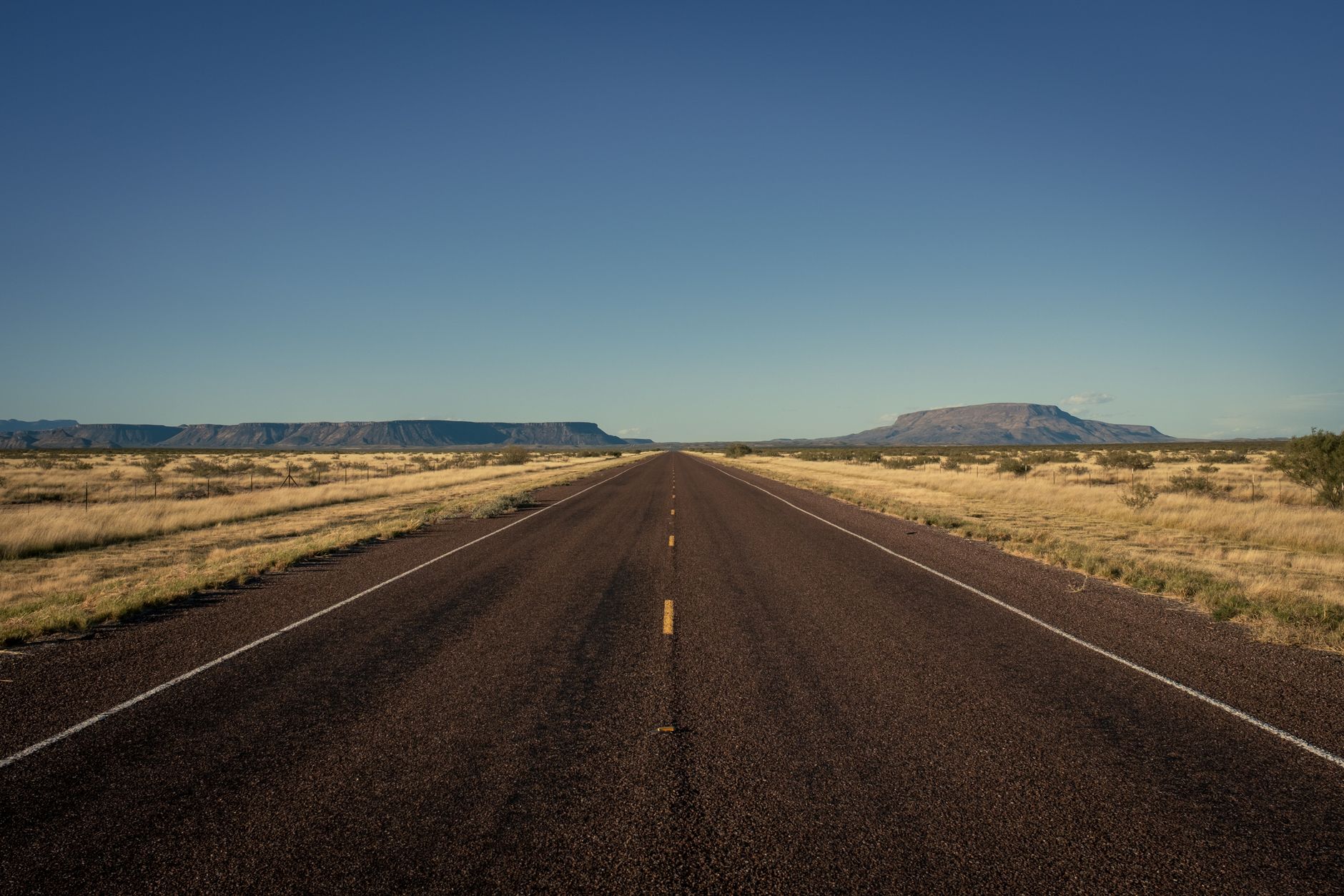 A tranquil desert highway stretching through Terlingua, Texas under a clear blue sky.
