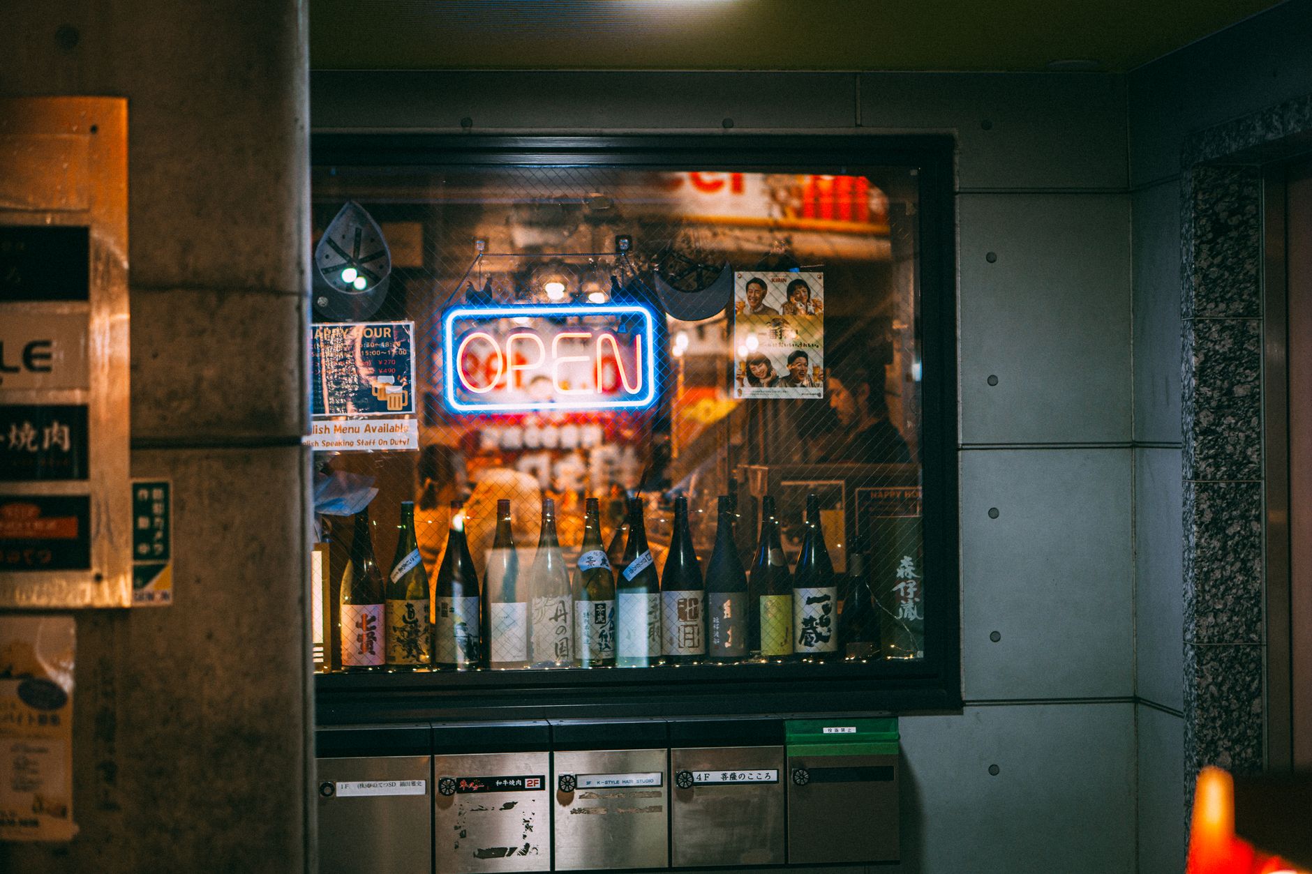 A cozy Japanese shop window displaying sake bottles and a vibrant neon open sign, evoking night ambiance.