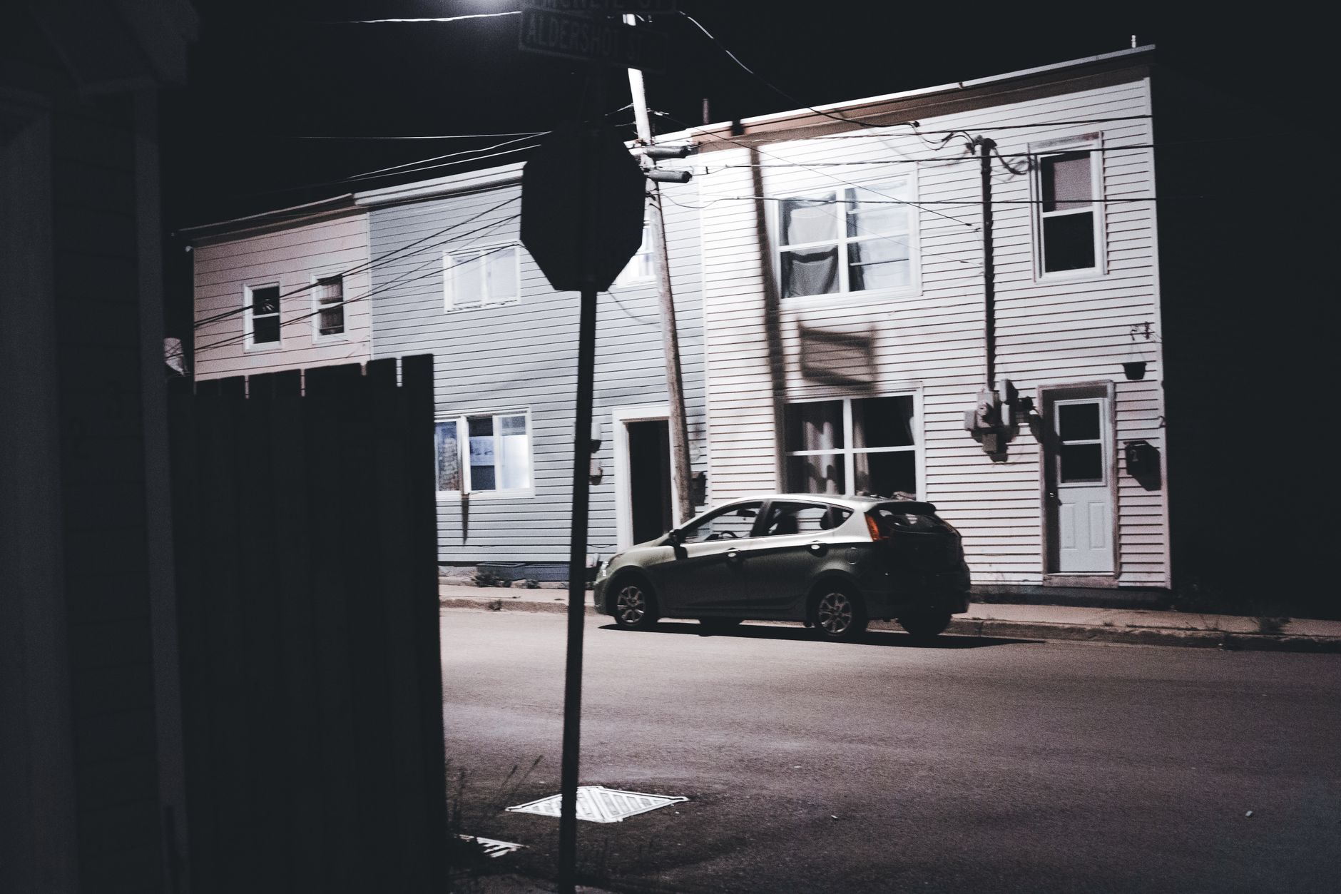 A hatchback car parked on a quiet, dimly lit street at night with urban housing background.
